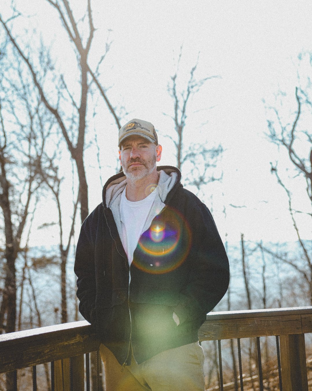 Portrait of Kevin Capehart on a wintery porch, wearing a West Virginia cap, bare trees behind him.